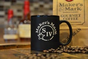 Close up picture of Makers Mark branded mug, next to coffee beans and branded gourmet coffee.